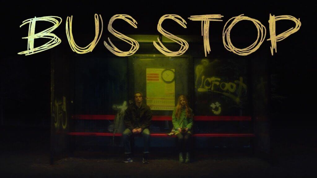 a boy and a girl sitting at a bus stop