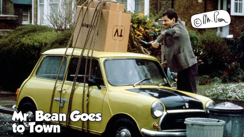 mr bean standing next to a green car loaded with boxes on its hood