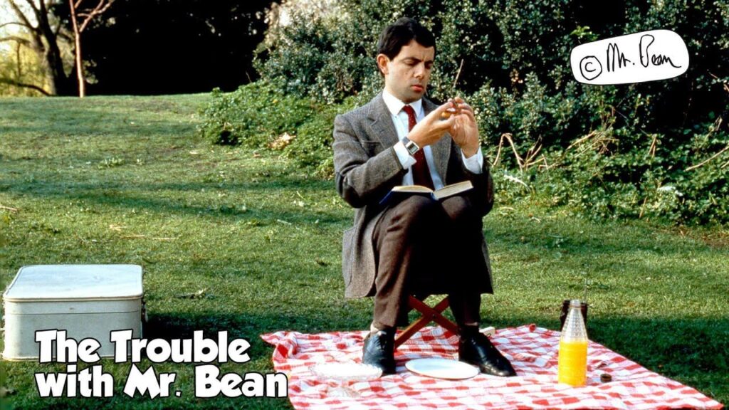 mr bean sitting in a park on a chair on a picnic blanket