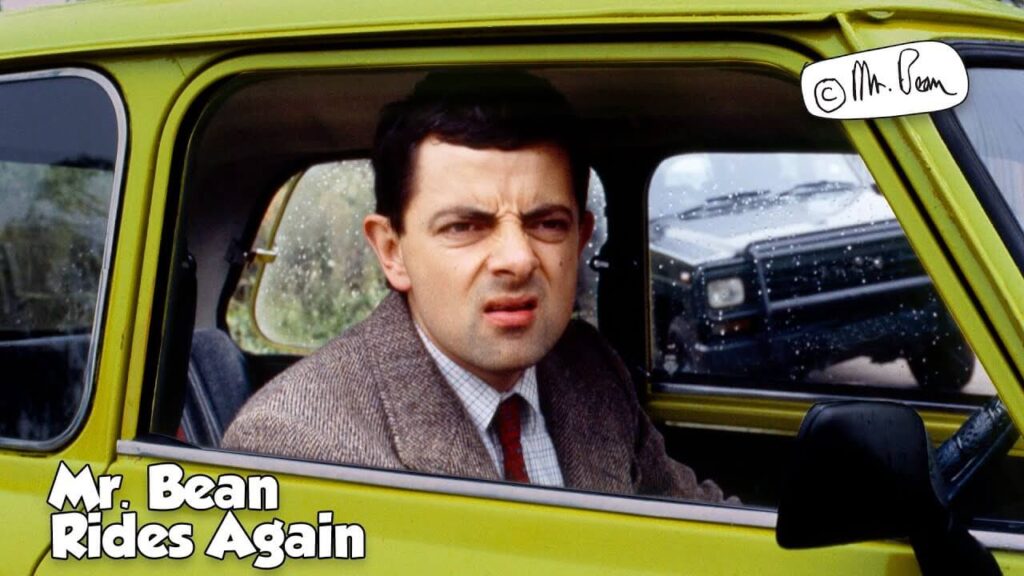 mr bean making a weird face while sitting in his green car