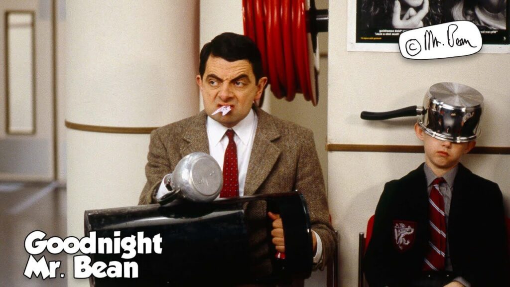 mr bean with a kettle stuck to his hand and a slip in his mouth sitting next to a boy with a cooker stuck to his head